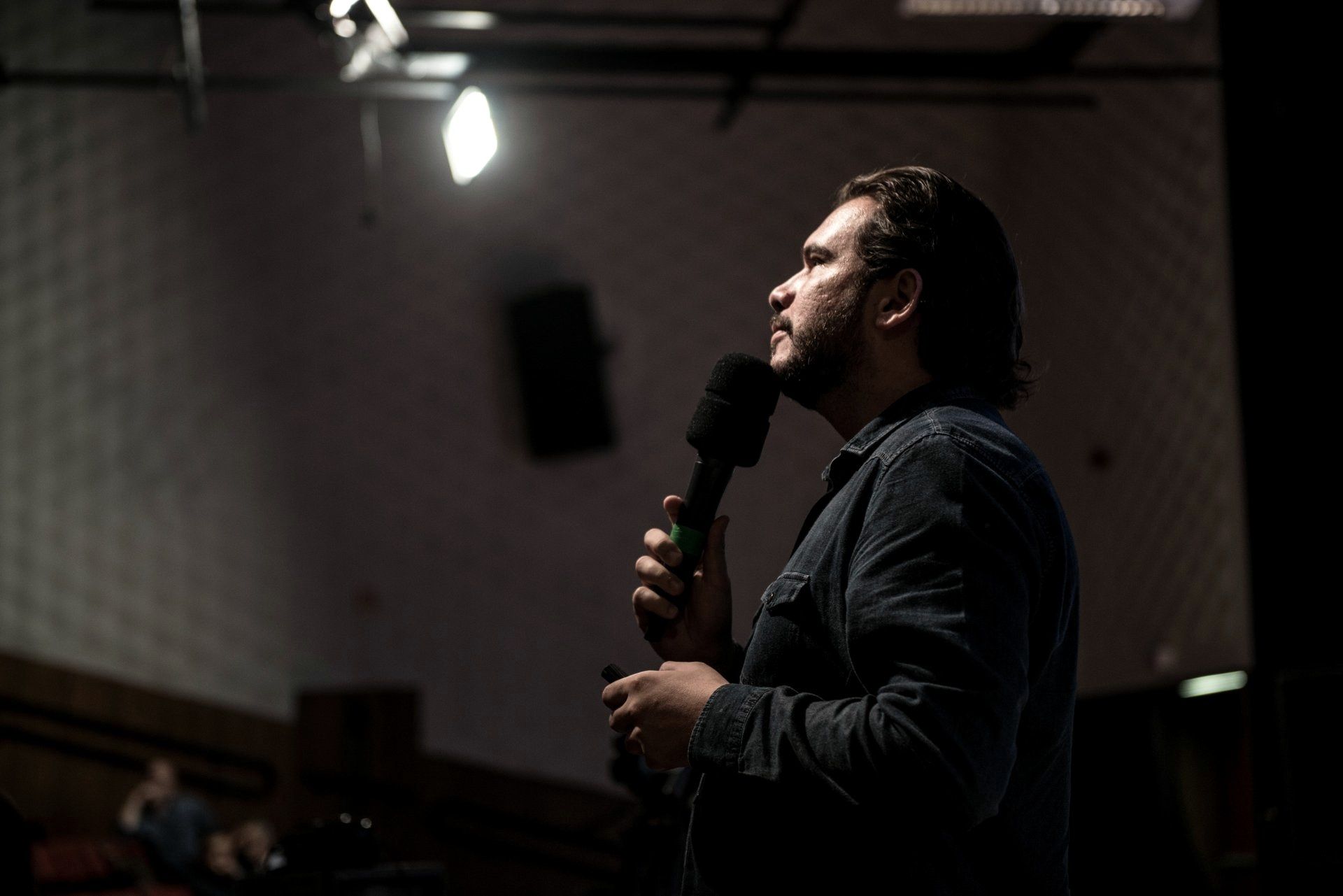 Fernando Palacios in profile on a darkened stage, microphone in hand